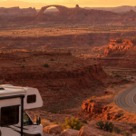 Wohnmobil auf einer kurvigen Straße in einer roten Wüstenlandschaft bei Sonnenuntergang