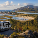 Panoramablick auf Küste, Hafen, Berge und Wasserfall; im Vordergrund steht ein Wohnmobil