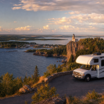 Wohnmobil an einer Küstenstraße mit Leuchtturm auf einer Klippe bei Sonnenuntergang