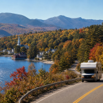 Wohnmobil auf einer kurvigen Uferstraße am See mit Herbstlaub und Bergen im Hintergrund